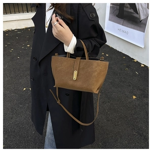 Detailed close-up of brown suede tote bag with gold oval clasp and adjustable strap