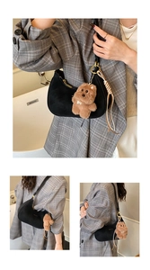 Detail of black crescent shoulder bag with plush bear charm and woven tassel accent