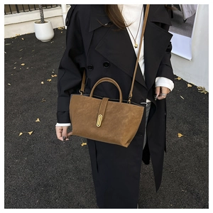 Detail of a brown suede handbag featuring a gold oval lock and textured matte finish