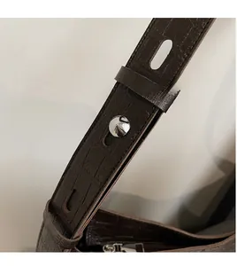 Detail of adjustable crocodile pattern strap with silver buckle on brown bucket bag