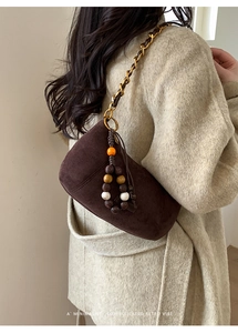 Détail du sac à bandoulière en daim marron avec chaîne dorée et pendentif perlé