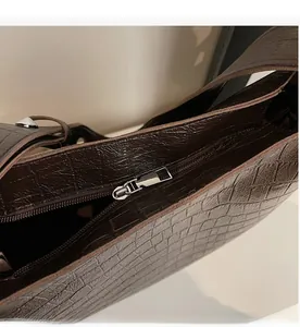 Close-up of smooth metal zipper and crocodile embossed texture on brown bucket bag