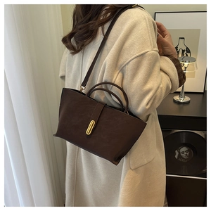 Detail of dark brown matte leather handbag with gold buckle shown on a beige coat