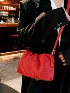 Red suede pleated cloud crossbody bag with shoulder strap worn by a model in a cafe