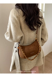 Sac demi-lune en daim marron minimaliste avec chaîne dorée sur un manteau beige