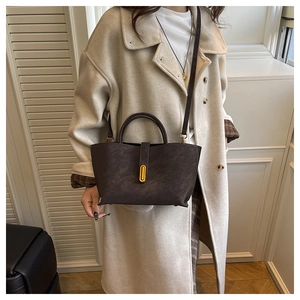Detail of dark brown matte leather tote bag with gold buckle hardware on beige coat