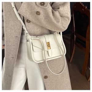 Détail d'un sac bandoulière crème minimaliste avec fermoir doré porté par un mannequin