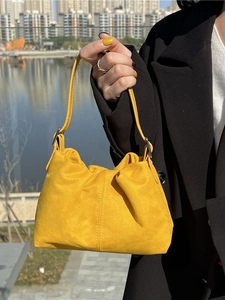 Yellow pleated bucket bag with top handle shown in a sunny outdoor setting