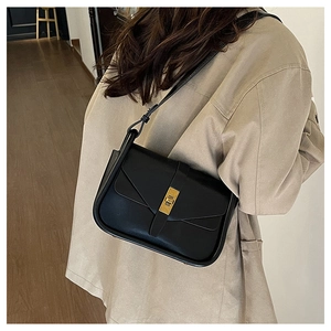 Détail d'un sac bandoulière noir avec boucle dorée sur une tenue beige chic