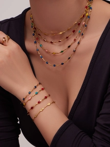 Detail of layered gold jewelry set with colorful enamel teardrop accents on a model