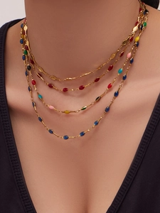Close-up of layered gold necklace set with colorful enamel drop pendants on model