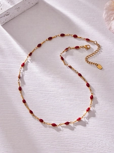 Detail of 18K gold-plated necklace featuring red enamel droplets on a stainless steel chain