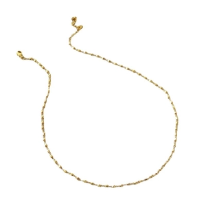 Collier minimaliste en perles dorées facettées avec chaîne fine sur fond blanc