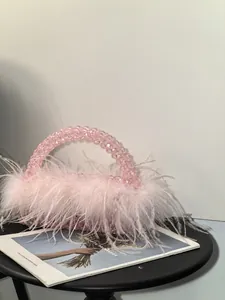 Detail of light pink beaded handbag featuring fluffy ostrich feather trim on a black table
