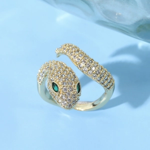 Macro view of crystal-encrusted snake ring with vibrant green gem eyes on blue background