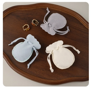 Three premium velvet jewelry drawstring pouches in grey, blue, and cream on a wood tray