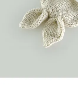Detailed close-up of cream white hand-knitted baby hat with cute ear design and texture