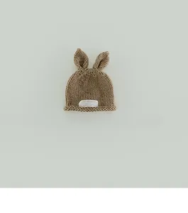 Detail of baby knit hat featuring 3D bunny ears and woven label on brown wool fabric