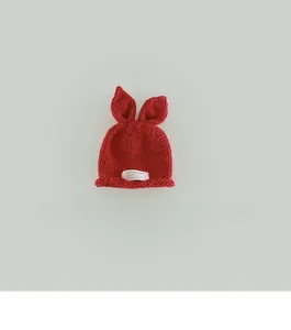 Detail of red hand-knitted baby hat with long rabbit ears and a white fabric label