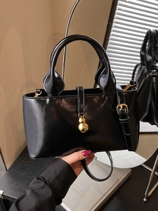 Glossy black patent leather handbag with gold gourd charm in a vintage interior setting