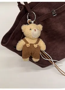 Detail of cute beige teddy bear charm in corduroy overalls on a brown tote bag