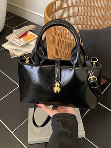 Glossy black leather tote bag with gold gourd pendant and adjustable shoulder strap