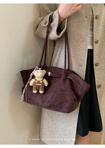 Detail of dark brown suede tote bag with plush bear charm worn over a beige coat