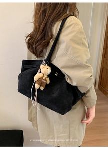 Detail of black suede tote bag with a cute bear charm and minimalist shoulder strap
