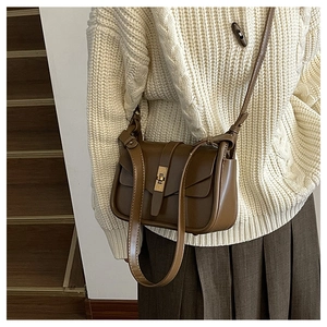 Détail d'un sac bandoulière vintage marron avec fermoir tournant doré sur un pull en maille