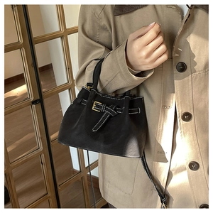 Détail d'un sac seau en cuir noir avec surpiqûres blanches et bandoulière sur un mannequin