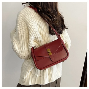 Détail du sac bandoulière en cuir bordeaux avec fermoir doré sur un pull d'hiver minimaliste