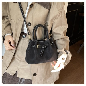 Détail du sac seau noir avec surpiqûres blanches et boucle dorée porté par un mannequin