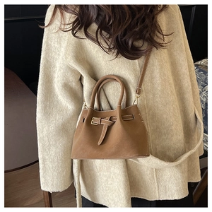 Brown bucket bag styled on a beige sweater, highlighting the strap and leather buckle detail