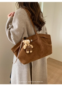 Detail of a brown suede tote bag with a cute bear charm on a minimalist grey coat
