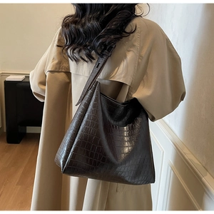 Detail of dark brown crocodile embossed shoulder bag on a model wearing a trench coat