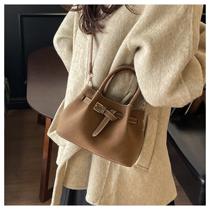 Brown suede crossbody bucket bag with buckle detail shown on a model wearing a beige wool coat