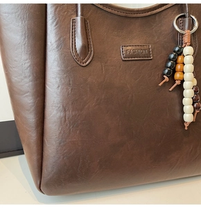 Détail du cabas marron foncé montrant la texture grainée et le pendentif en perles de bois