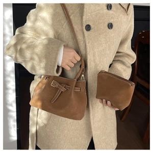 Brown suede crossbody bucket bag with decorative buckle and matching coin purse on beige coat