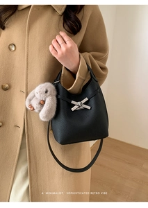 Detail of black lychee grain bucket bag with metal clasp and plush rabbit charm
