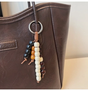 Détail d'un pendentif en perles de bois colorées sur un sac fourre-tout en cuir brun