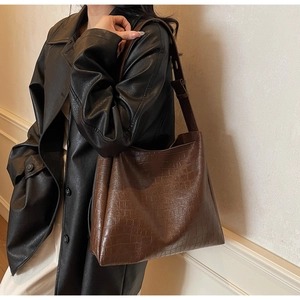 Close-up of deep brown crocodile texture leather tote bag on model in black trench coat