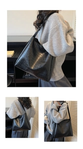 Detail view of large black tote bag featuring crocodile embossed texture and long strap