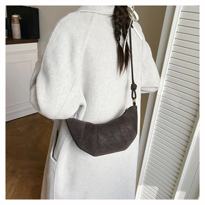 Détail d'un sac demi-lune en daim marron foncé montrant sa texture plissée et ses nœuds