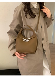 Brown lychee leather bucket bag with silver buckle worn by model in khaki coat