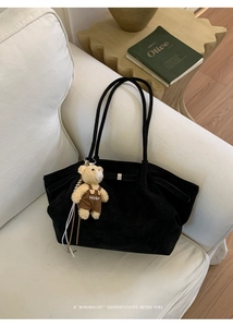 Detailed texture of black suede tote bag with a cute plush bear charm on a white sofa