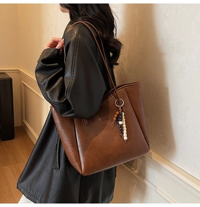 Détail d'un grand sac cabas en cuir marron avec un pendentif décoratif en perles