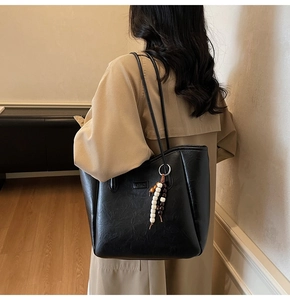 Detail of black faux leather tote bag with wooden bead charm and FASHION logo tag