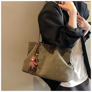 Close-up of suede tote bag featuring contrast stitching and a cute bear bag charm