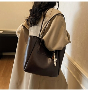 Vue détaillée du grand sac cabas marron foncé avec pendentif en perles sur un trench
