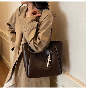 Détail d'un grand cabas en cuir marron foncé avec un gland perlé sur trench-coat
